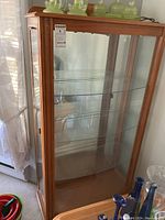 Front view of oak curio cabinet showing glass shelves and wood frame with carved trim