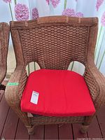 Front view of a brown wicker deck chair with red seat cushion, showing woven wicker detail and shape of chair.