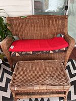 2-seater wicker deck settee with red cushion and floral cushion underneath. Wicker coffee table in front.