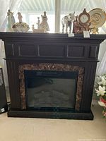 Full front view of the dark wood electric fireplace with decorative paneling and faux marble trim around the firebox with artificial logs inside.
