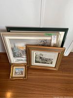 Set of four assorted framed canvas paintings leaning against a wall, showing varying frame styles and sizes.