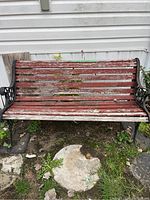 Full view of weathered red wooden slatted garden bench with black metal decorative armrests and legs, showing chipping paint and outdoor wear.