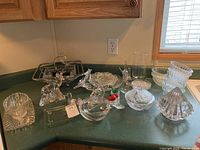 Photo of assorted clear glassware including bowls, candy dish, trays, and figurines arranged on kitchen counter.