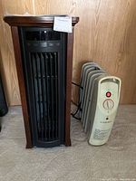 Photo showing two heaters side by side on carpet floor: Duraflame electric heater in wood-tone frame and black front, Airworks off-white oil-filled radiator heater with control dial and red light