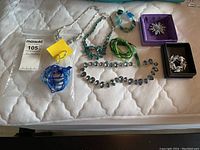 Overview of all jewellery pieces laid out, showing necklaces, bracelets, brooches, and earrings mostly in blue and green tones.