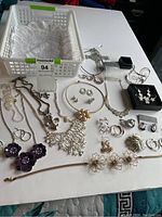 Overview of assorted jewellery pieces spread on a table including necklaces, earrings, brooches, and boxed pairs of earrings.