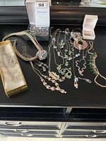 Overhead view of assorted jewelry on a black surface including multiple necklaces, bracelets, earrings, and a brooch.