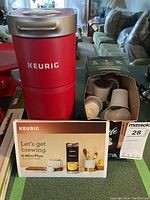 Red Keurig K-Mini Plus coffee maker with McCafe coffee pods in box and Keurig quick start guide booklet.