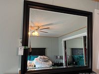 Front view of the large black wood frame mirror hanging on a wall reflecting room interior.