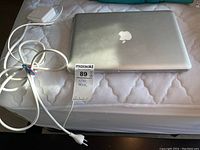 Closed silver MacBook Pro with MagSafe power adapter and cable on mattress