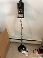 Full view of metal detector standing upright showing control unit, shaft, and search coil on floor, with owner's manual placed on the floor.