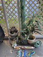 Full shot of all outdoor items showing artificial plant, rolled rug, garden decor, water feature and wall art.