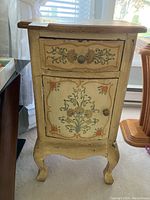 Front view of the decorative painted wooden table showing drawer and cabinet door with floral designs and cabriole legs.