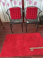 Two black metal patio chairs with red tufted cushions and a large red shaggy rug in front.