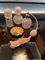 Front view of three pink textured glass perfume bottles and vintage brass compact on dark reflective surface