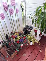 Various real and fake plants, pots, black lanterns, and a decorative metal plant holder photographed in corner with white curtain background.