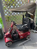 Side profile of red Fortress 1700 Series scooter showing canopy, seat, body and metal support bar on floor