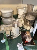 Photo showing all appliances arranged on counter: Black & Decker Flavor Scenter Herb Steamer, Braun Juicer, Black & Decker Food Processor with manual, Homemax Hand Mixer, Black & Decker Hand Mixer, and Salton Coffee Grinder with power cords and attachments visible.