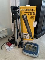 Bushnell Sportview Zoom 60mm telescope box, Velbon CX 540 tripod, Nikon Coolpix camera, small Bushnell binoculars, and digital clock thermometer calendar on carpet