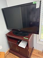 Front angled photo showing Sharp 40 inch TV on wooden cabinet stand with remote and some papers on shelf.