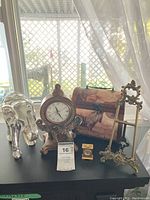 Wide view of lot items displayed on table near window showing silver elephant, elephant clock, wooden box, small brass clock and metal decorative stand.