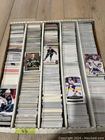 Photo showing a large box with approximately 5000 hockey base cards divided into five rows. Cards feature various hockey players mainly from the 2010s with some from the 1990s. Cards are standard size and ungraded.