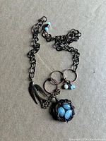 Photo of a bird and nest necklace with dark metal chain and blue bead eggs in a wire nest pendant