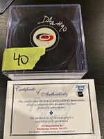 Photo of signed Carolina Hurricanes hockey puck in clear plastic display case with yellow label '40' taped on the case, showing David Ayres autograph and certificate of authenticity card underneath.