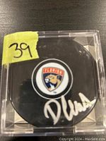 Signed hockey puck in a clear display case with visible crack on the side, featuring Florida Panthers logo and Devon Levi's autograph.