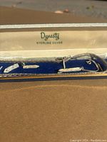 Close-up of the Dynastie marked sterling silver jewelry case with blue interior lining and silver jewelry inside.