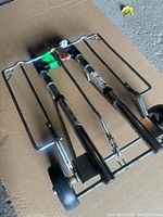 Photo of the foldable hand cart lying flat in a folded position showing metal frame and wheels.