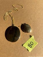 Photo of two gold plated lockets and one gold plated chain laid flat on beige surface with lot number mark.