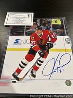 Photo of Jeremy Roenick skating on ice in Chicago Blackhawks uniform, signed in blue ink, with accompanying certificate of authenticity on top left corner and protective sleeve.
