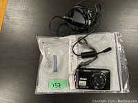 Photo showing Nikon Coolpix digital camera and a charger with cable laid on a black surface with plastic bag underneath.