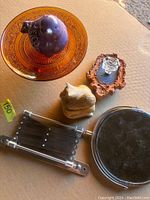 Lot of items on a cardboard surface including bronze tray, two bird sculptures, mirror, and metronome.