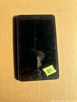 Front view of black Samsung tablet showing touchscreen and physical home button. Screen is off and reflects light.