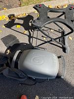 Weber electric BBQ components on pavement: plastic stand base, electric grill body, grilling plates and carrying bag, with autumn leaves around.