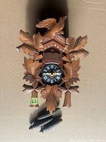 West German cuckoo clock with wooden carvings and metal weights.