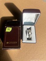 Citizen branded watch box containing a small women's wristwatch with metal bracelet, accompanied by paperwork inside the box lid.