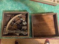 Open wooden box with brass sextant and loose box parts inside.