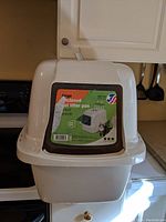 Front view of the white enclosed cat litter box with a brown framed flap door and the brand sticker visible on the front.