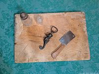 Antique wooden cutting board with knife marks, accompanied by small cleaver, seahorse-shaped bottle opener, and glass shaker on top.