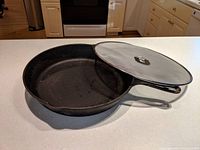Side angled view of Lodge cast iron skillet with Ikea splatter screen resting on the skillet edge on kitchen countertop.
