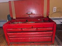 Front view of large red steel toolbox with drawers open and some tools visible