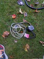 Little Giant fountain pump and attached hose laid on grass with fallen leaves.