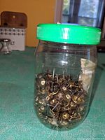 Plastic jar filled with round vintage upholstery nails with brass finish.