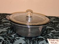 Side view of Pyrex Flameware covered casserole dish in pale blue glass with clear glass lid on black textured fabric.
