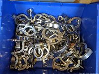 Blue bin filled with numerous stainless steel heavy duty sanitary tri-clamps, showing a large quantity and various hinged clamp designs.