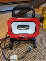 Front view showing red housing, LED grid, Snap-On branding, handle, and attached power cord.