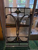 Front view of antique stained glass panel showing textured clear glass with decorative leaded floral motif and amber bands, held in acrylic frame in front of window.